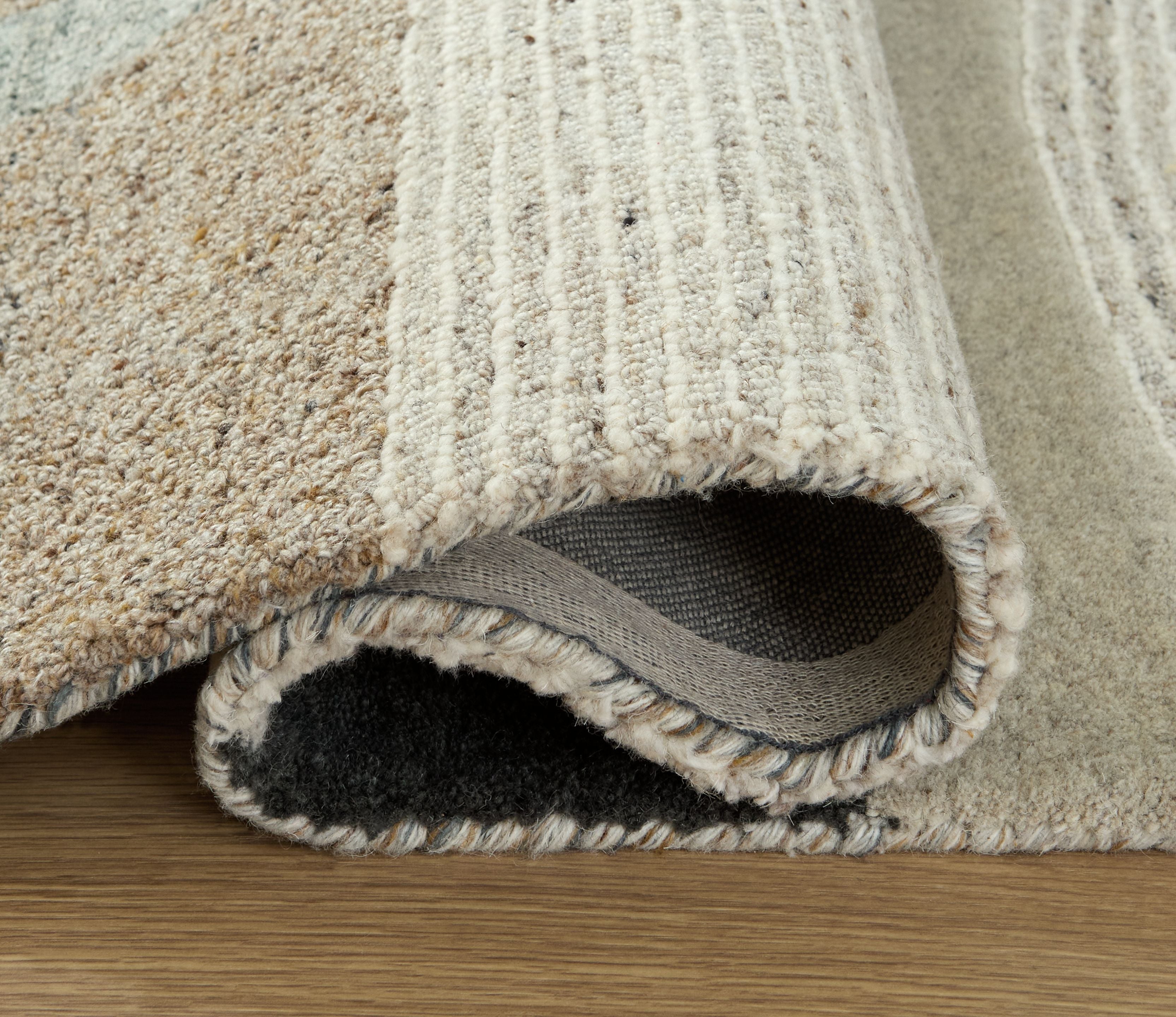 Beige area rug edge with short fringe and visible backing; textured looped fibers along border