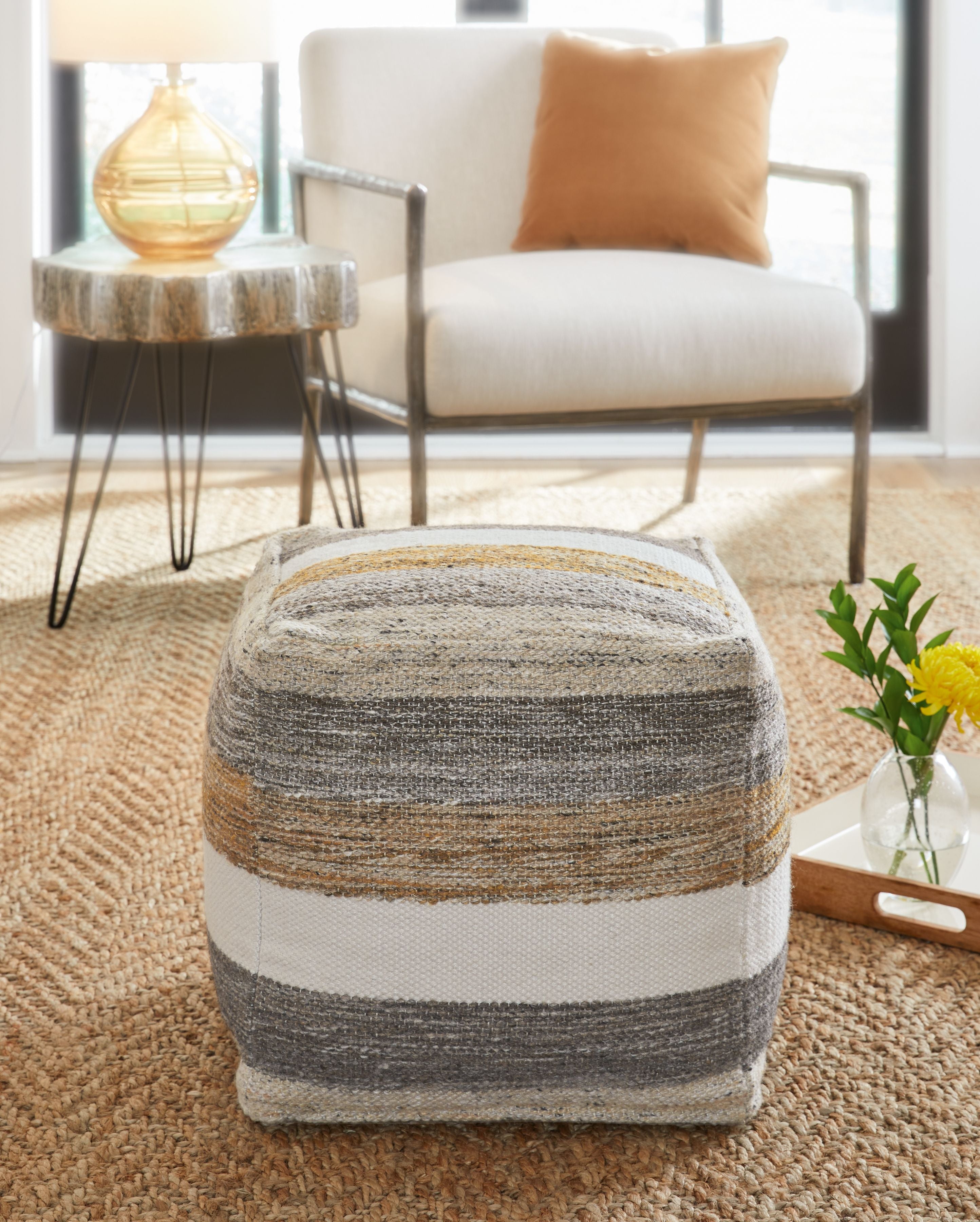 Striped fabric pouf with gray, white, and tan bands, square top.