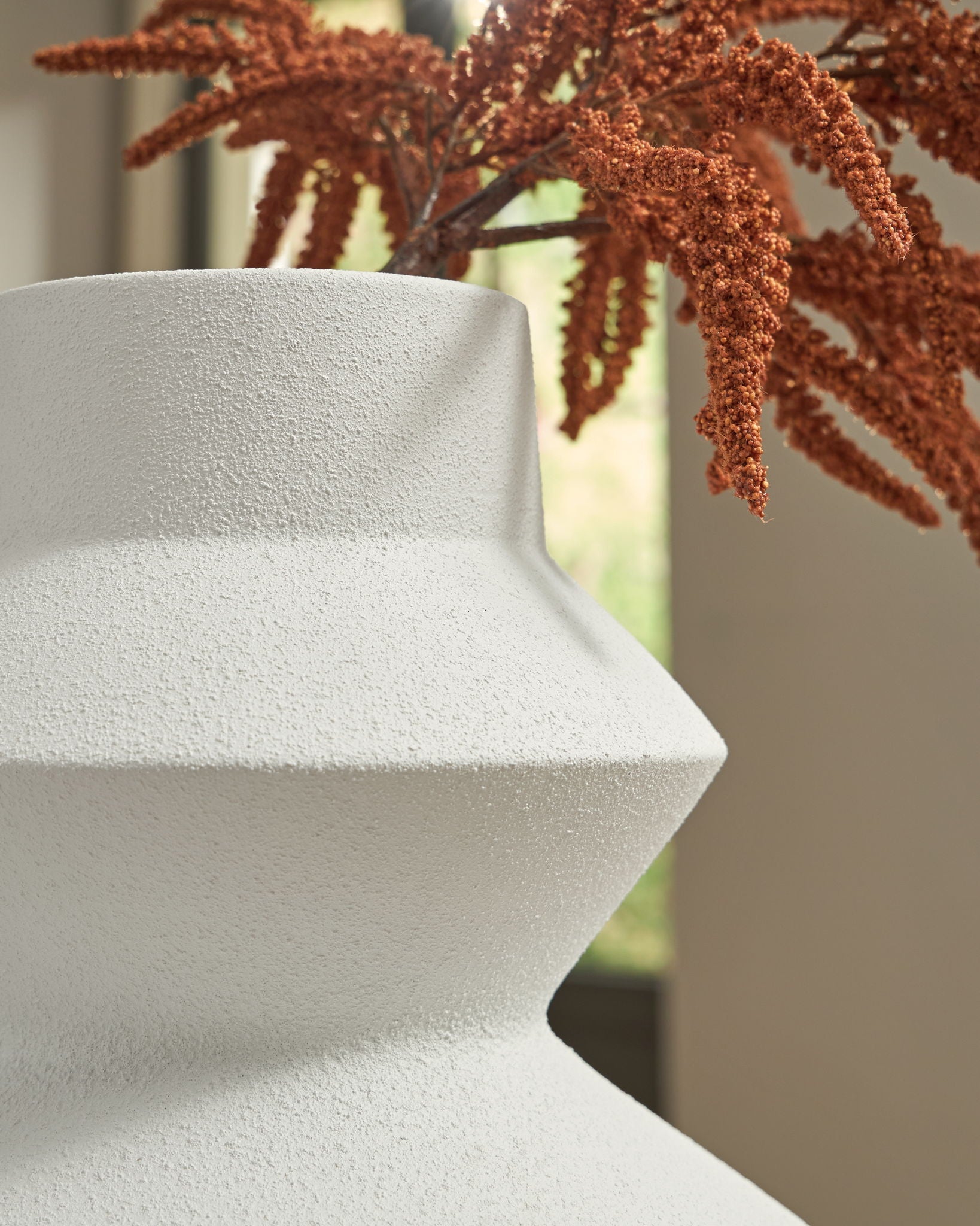 White ceramic vase with flared neck holding brown faux stems
