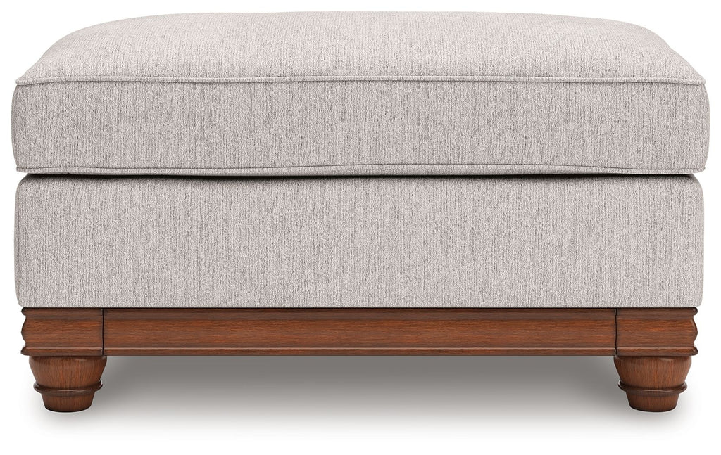 Sandstone upholstered ottoman with padded top and wooden trim base with turned feet