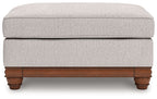 Sandstone upholstered ottoman with padded top and wooden trim base with turned feet