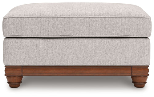 Sandstone upholstered ottoman with padded top and wooden trim base with turned feet