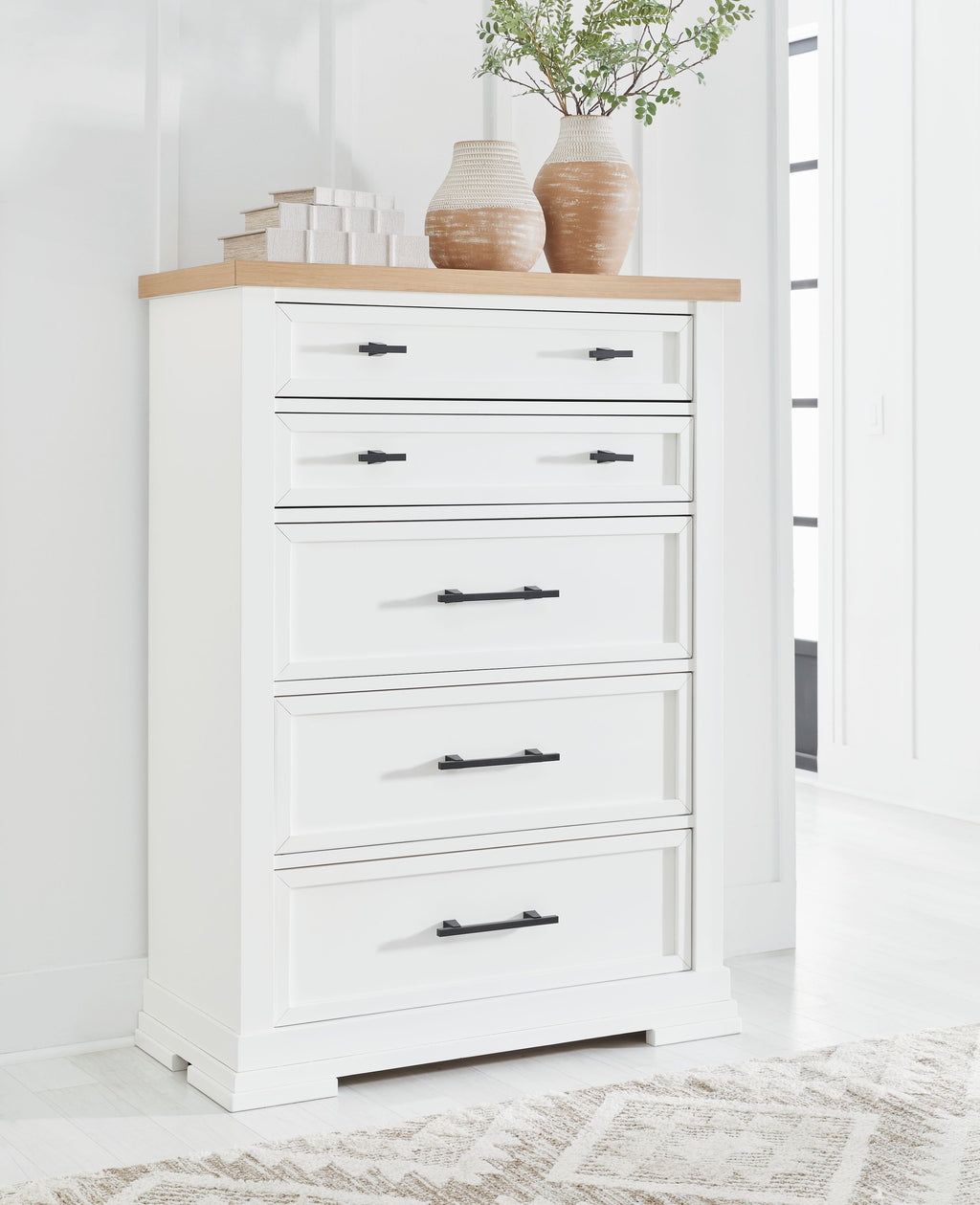 White five-drawer chest with black bar handles and items on the top