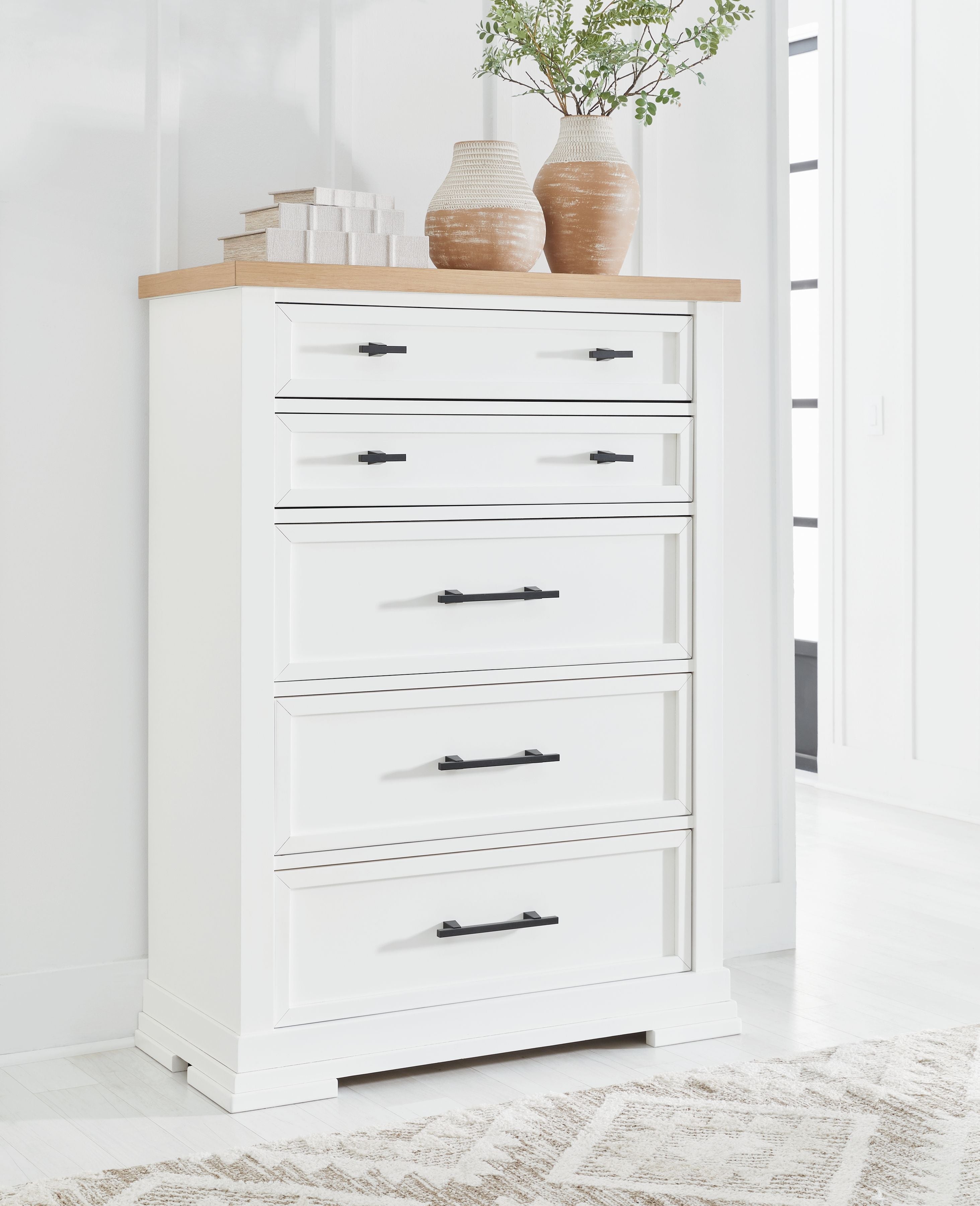 White five-drawer chest with black bar handles and items on the top