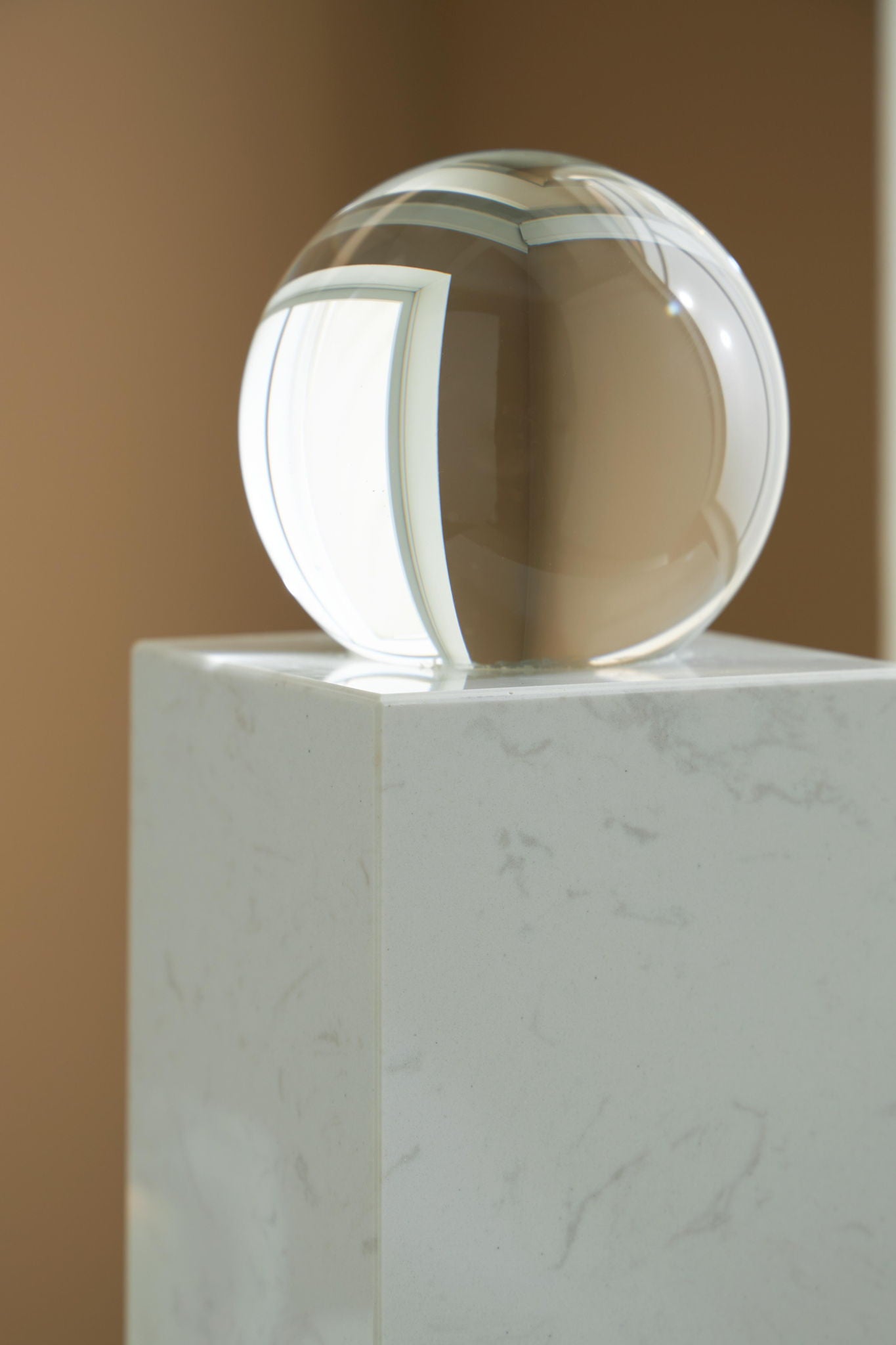 White glass sphere on white marble pedestal, close top angle