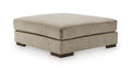 Square upholstered ottoman with thick cushion and dark legs, dune beige fabric.