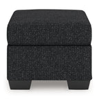 Upholstered ottoman with dark textured fabric, padded top, and short legs