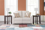 Light beige reclining loveseat with two geometric patterned throw pillows