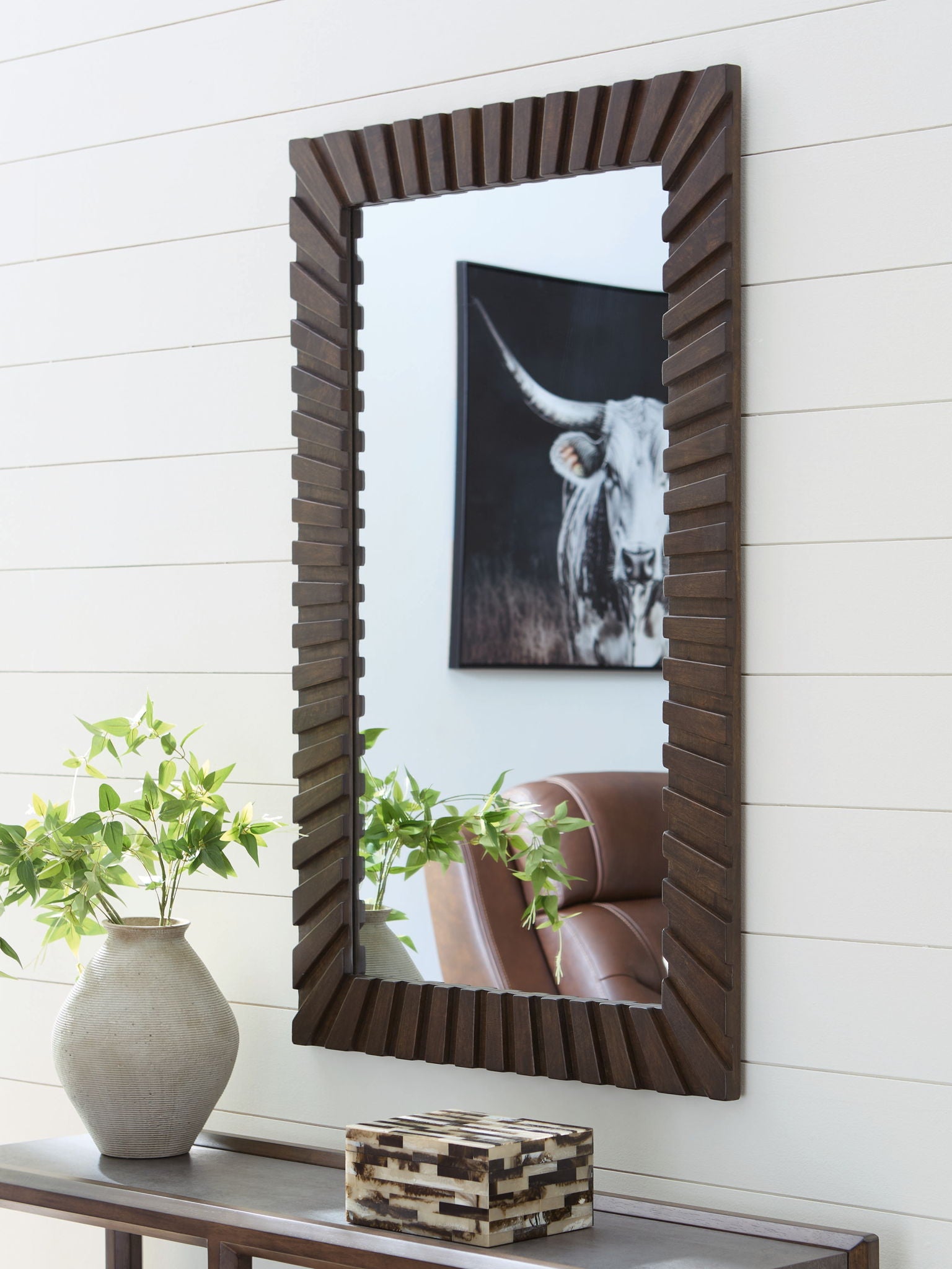 Dark brown slatted accent mirror reflecting a framed photo and room scene