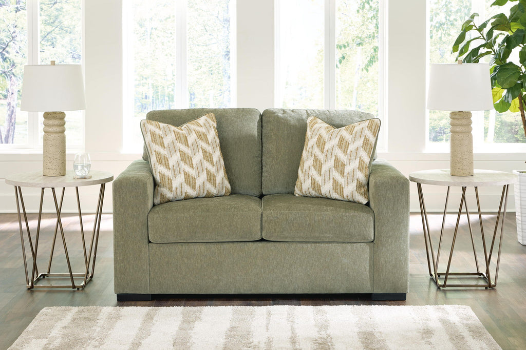 Olive green upholstered loveseat with two patterned accent pillows and square arms