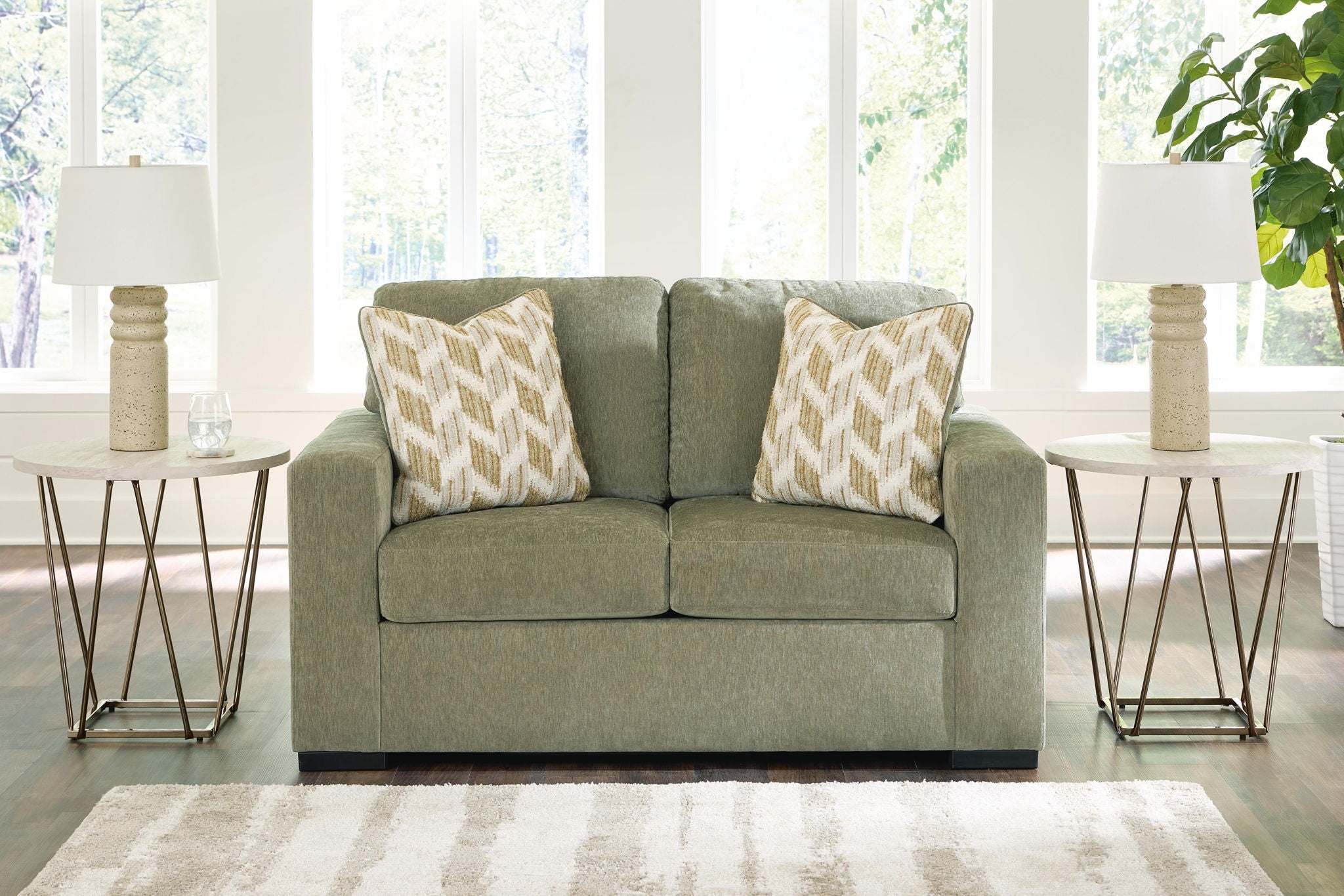 Olive green upholstered loveseat with two patterned accent pillows and square arms