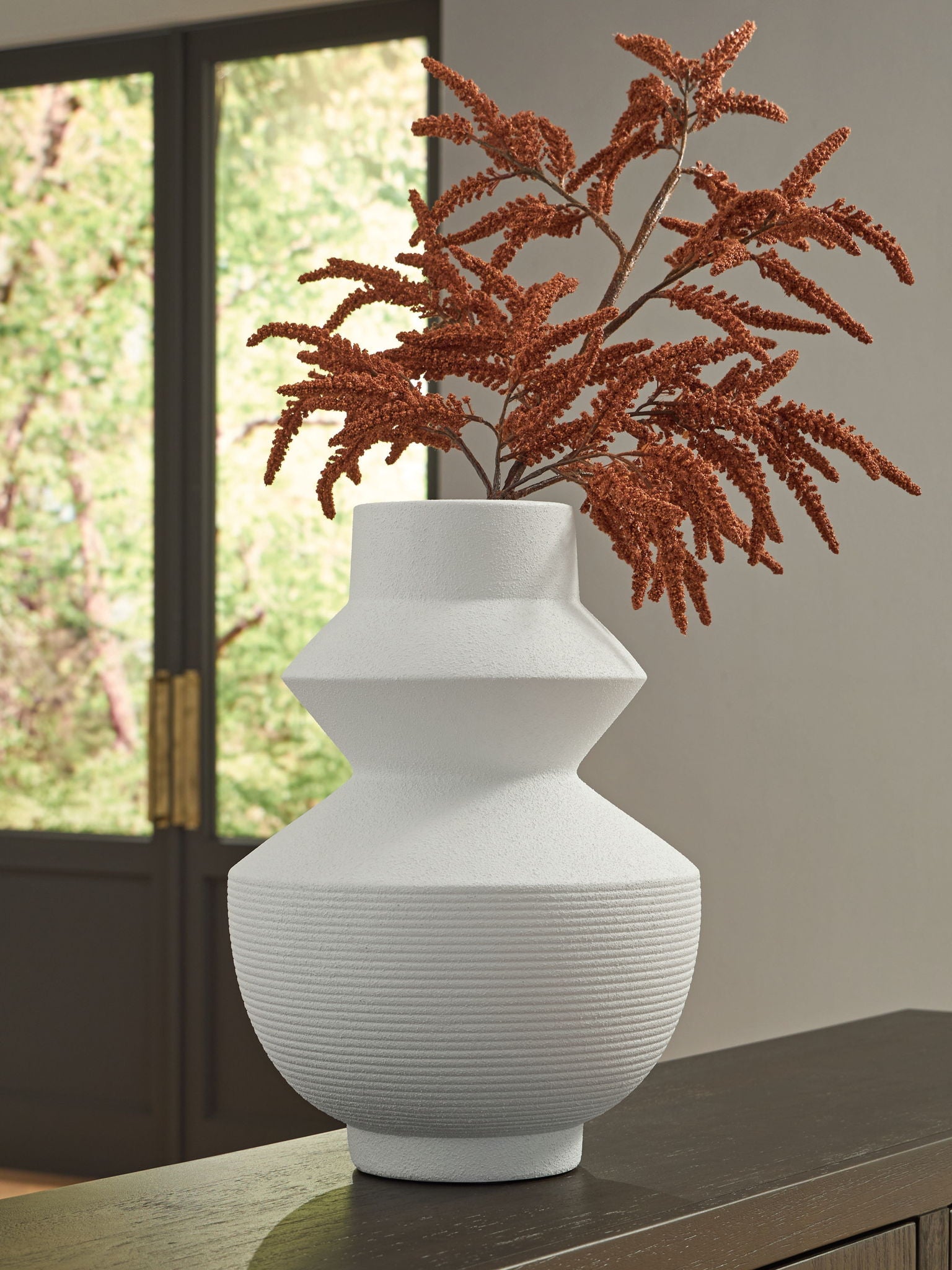 White ceramic vase on table with ribbed base and brown faux foliage