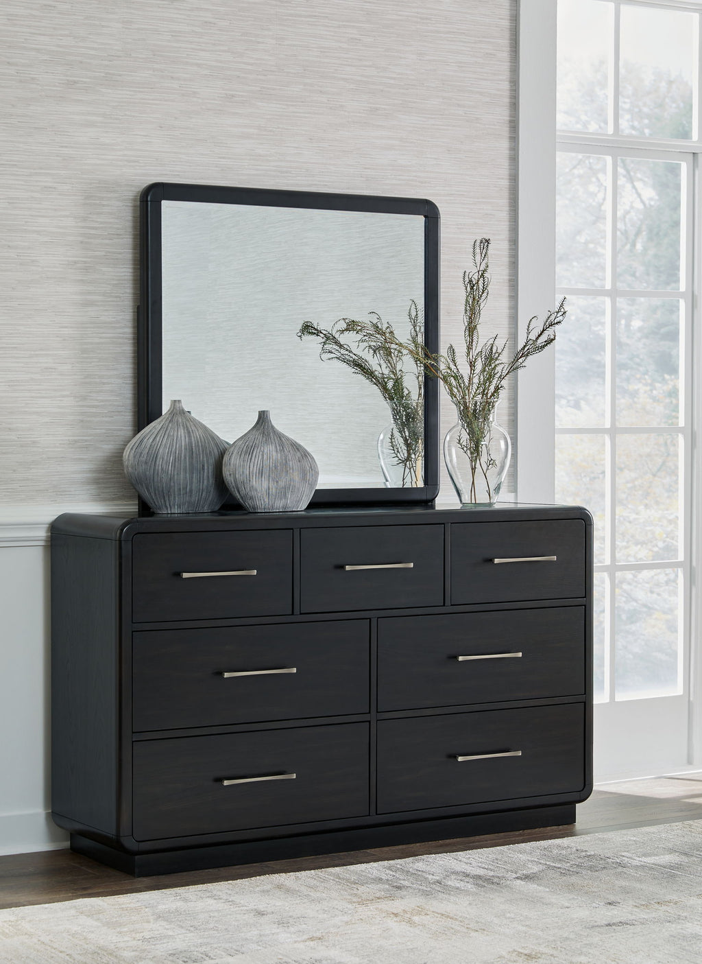 Black dresser with six drawers and metal bar handles, framed mirror