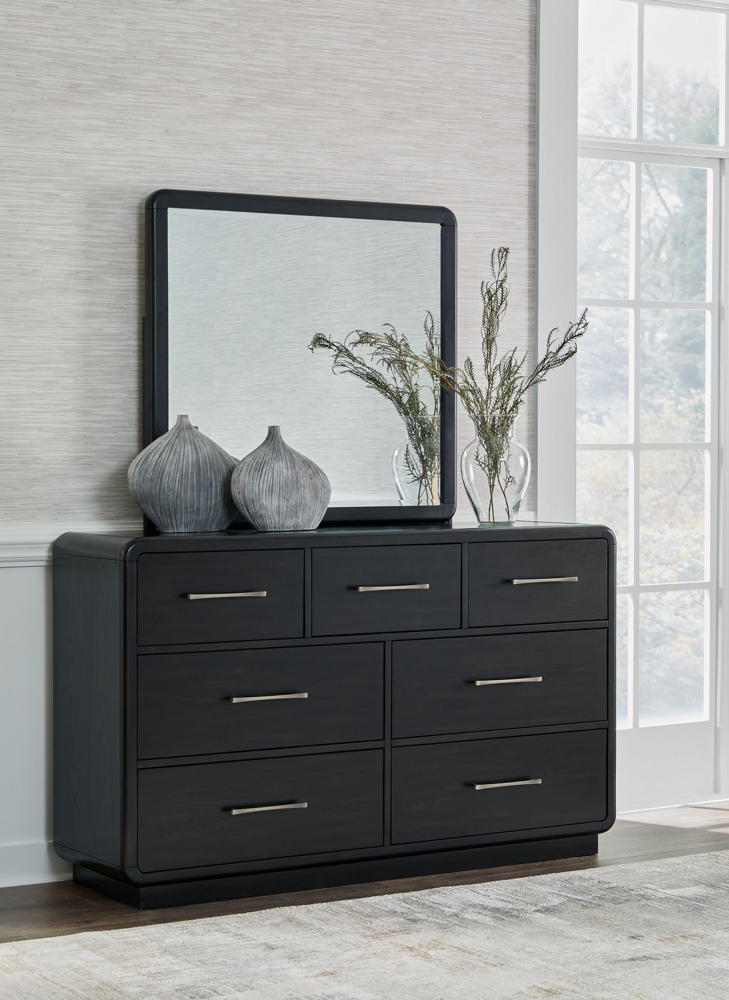Black dresser with six drawers and metal bar handles, framed mirror