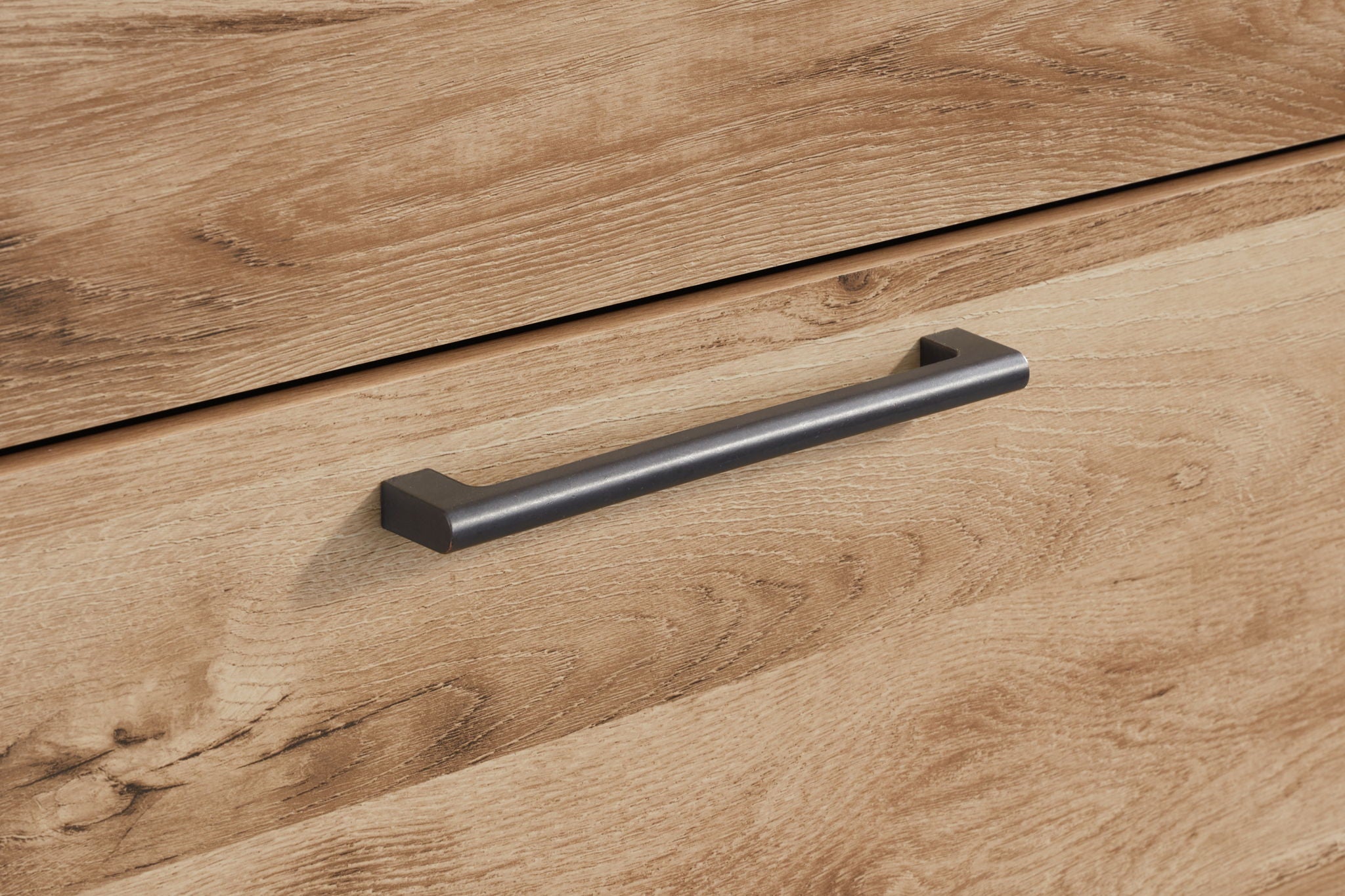 Dark metal dresser drawer pull on tan wood drawer front