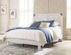 White panel bed with blue and beige pillows and quilt, supported by dark legs