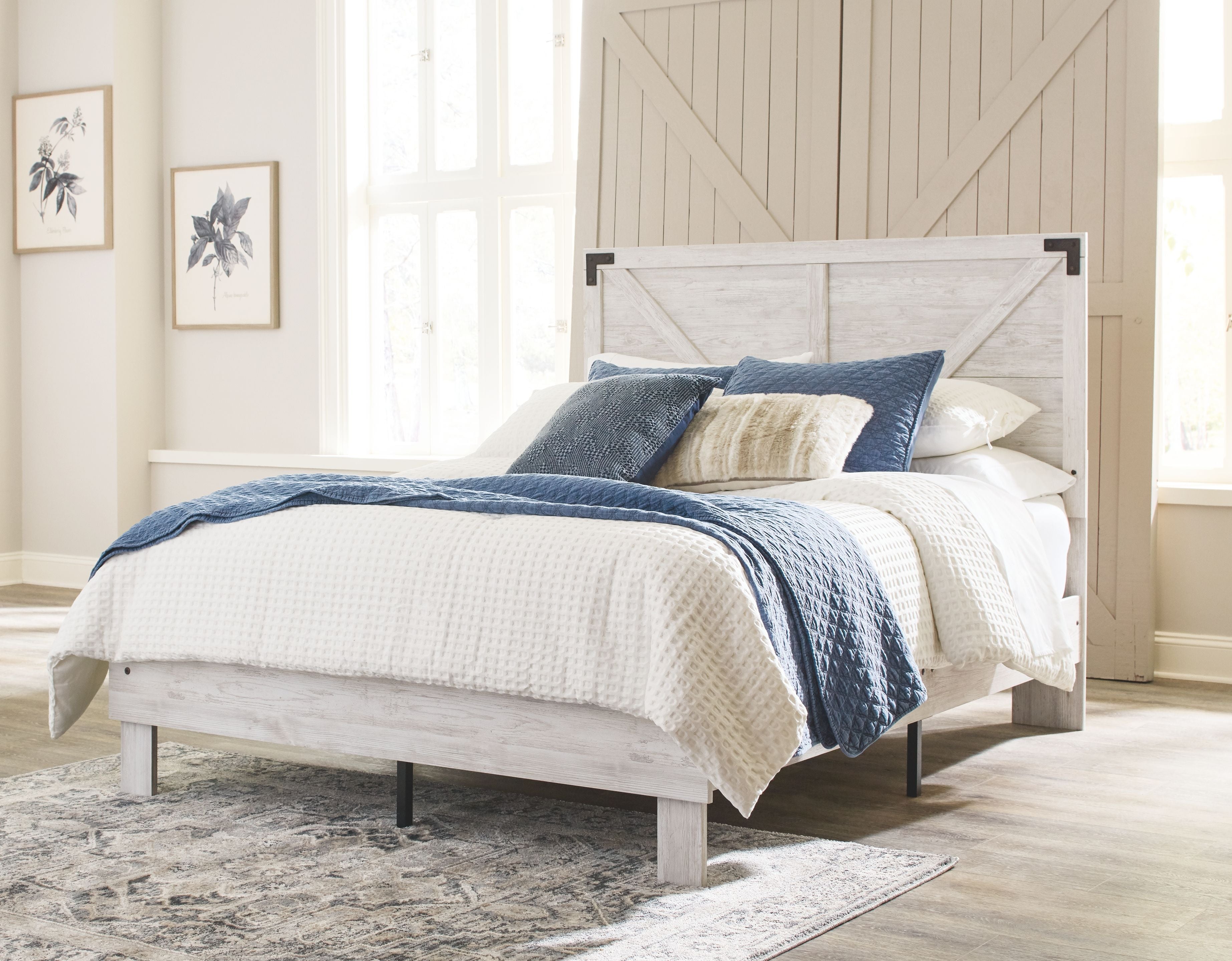 White panel bed with blue and beige pillows and quilt, supported by dark legs