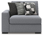 Gray upholstered corner chair with thick armrests, black legs, and three patterned cushions
