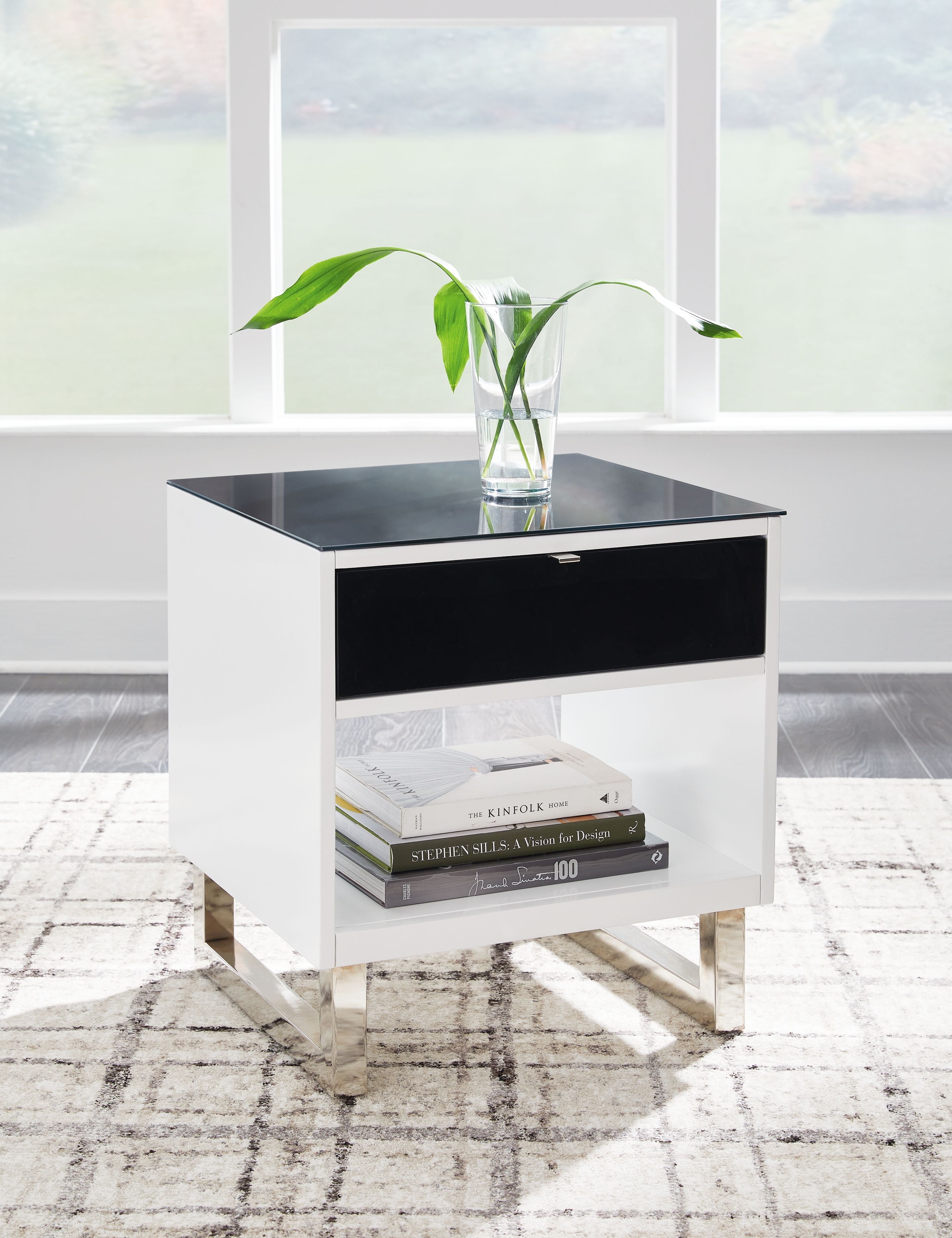 Rectangular end table with black top and drawer, white body, books on lower shelf