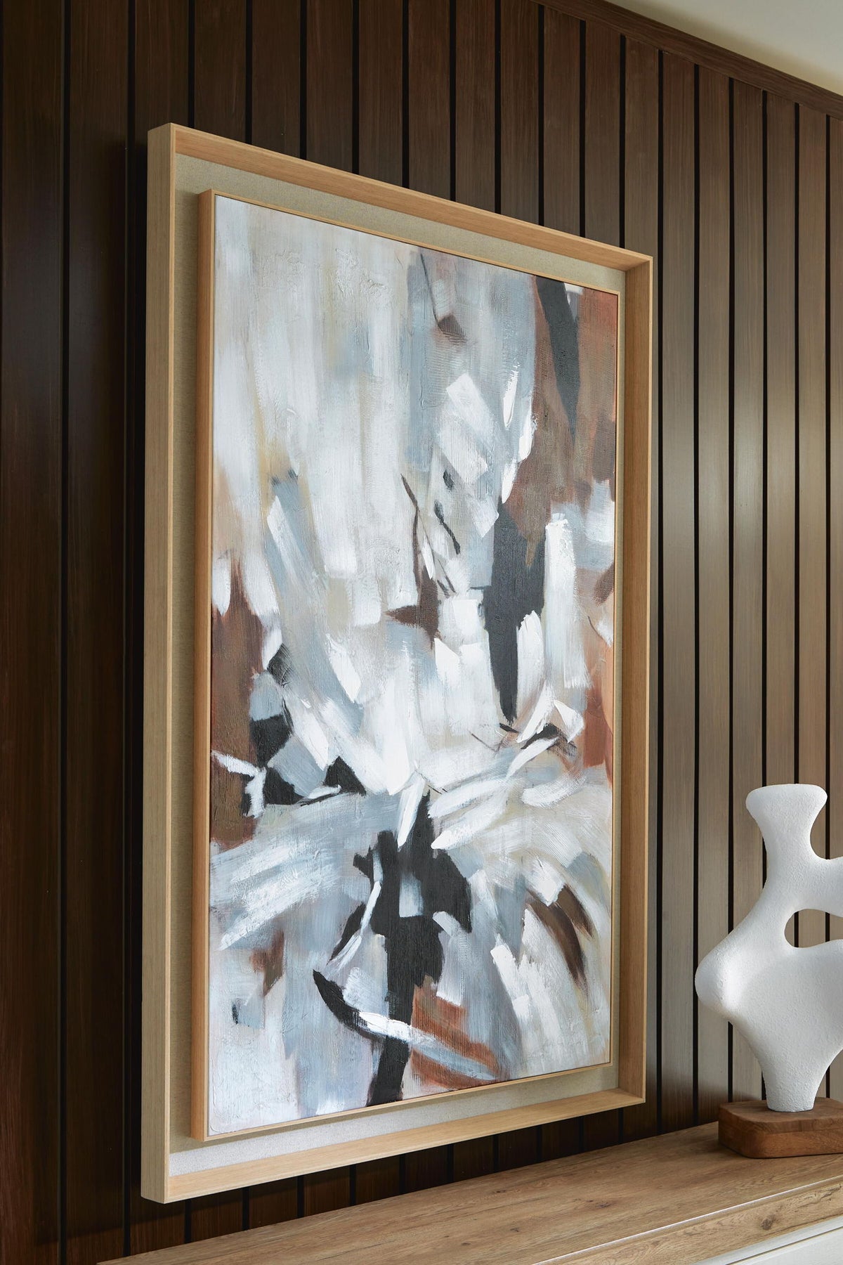 Framed abstract wall art with white and black brushwork in a light wood frame