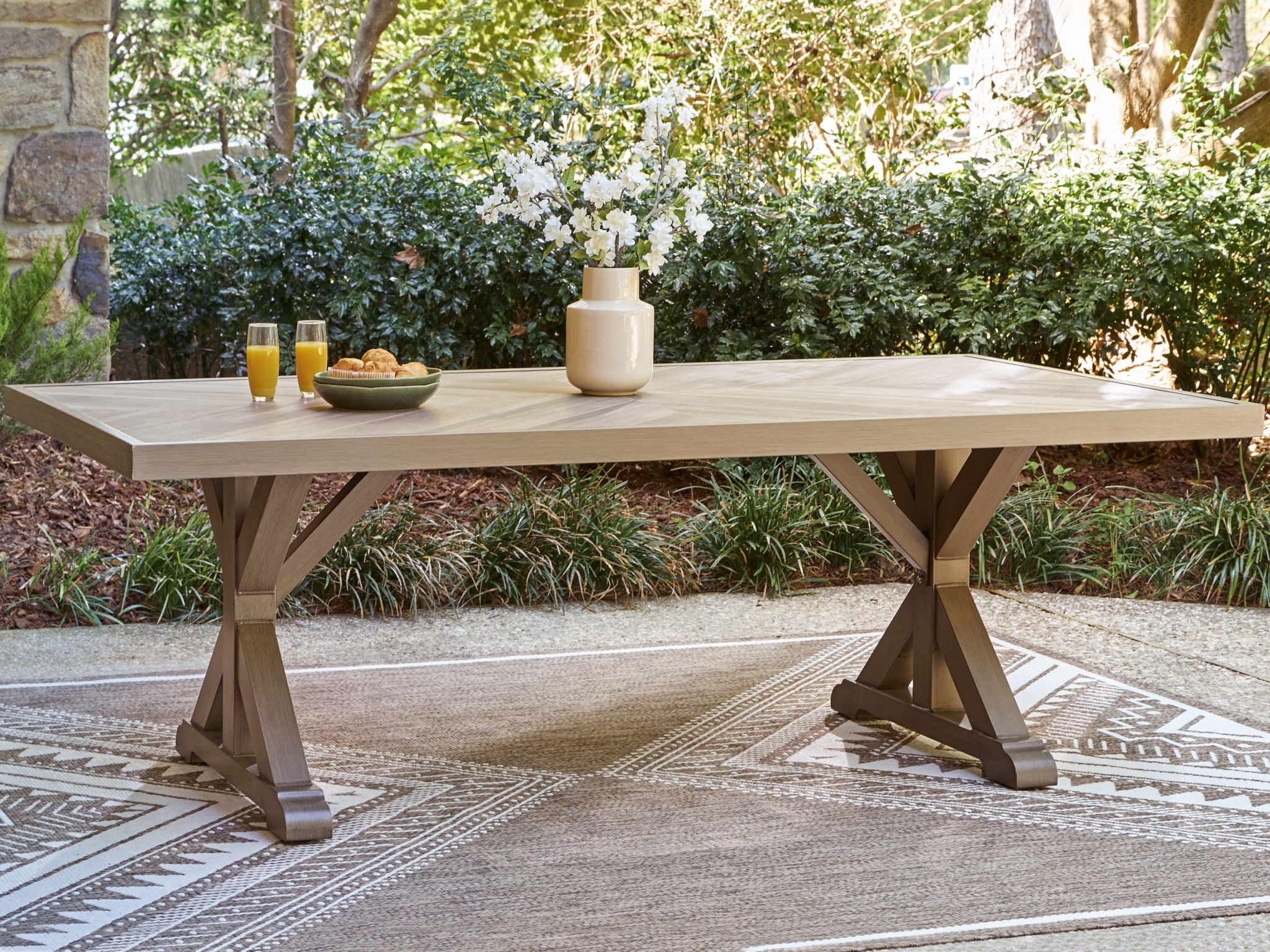 Rectangular dining table with slatted beige top and pedestal X legs.