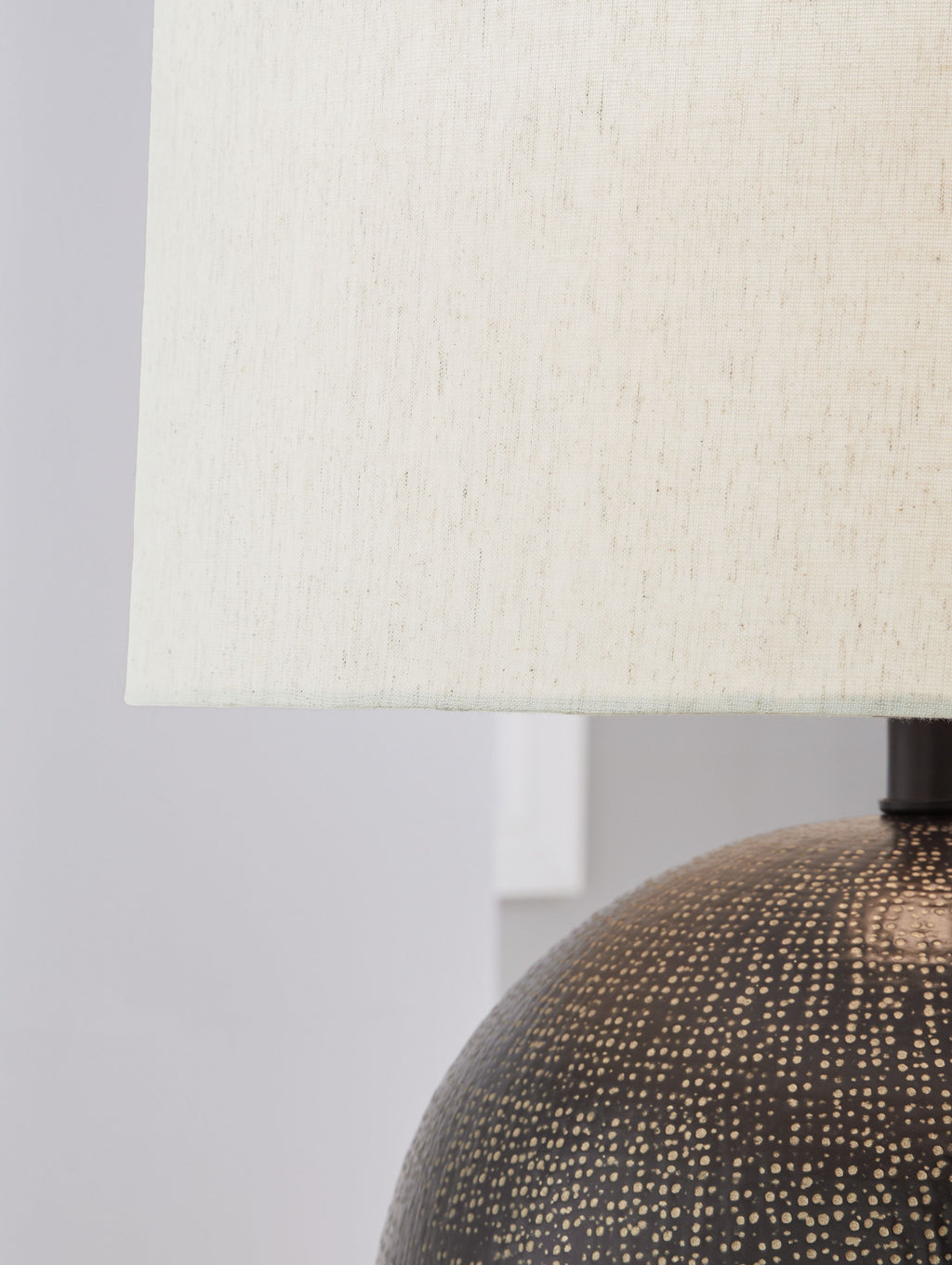 Beige fabric lampshade with dark neck mount and top of dark speckled globe base