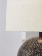 Beige fabric lampshade with dark neck mount and top of dark speckled globe base