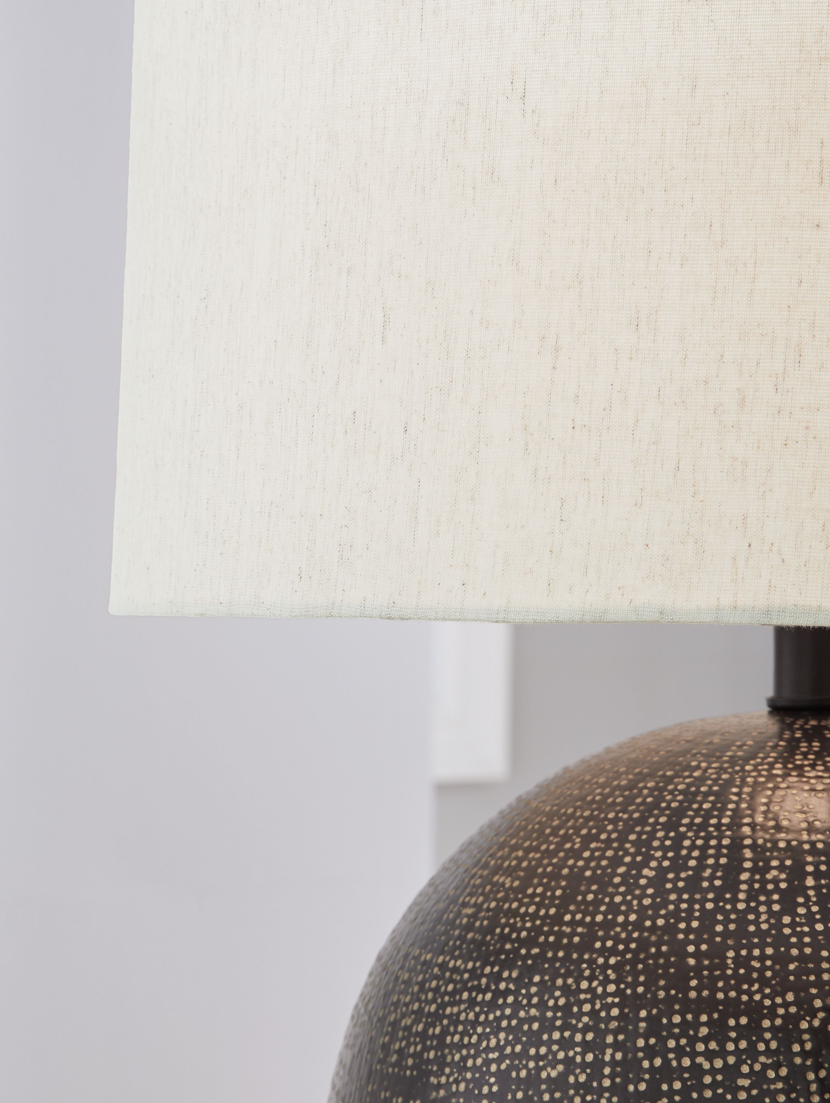 Beige fabric lampshade with dark neck mount and top of dark speckled globe base
