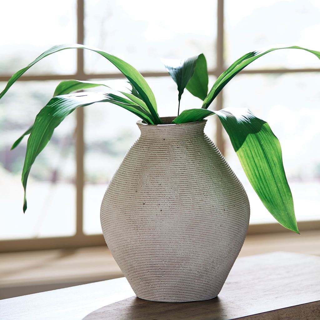 Beige ceramic vase with fine texture and wide rounded body holding greenery