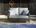 Gray wicker loveseat with seat cushions, back cushions, and patterned pillows outdoors