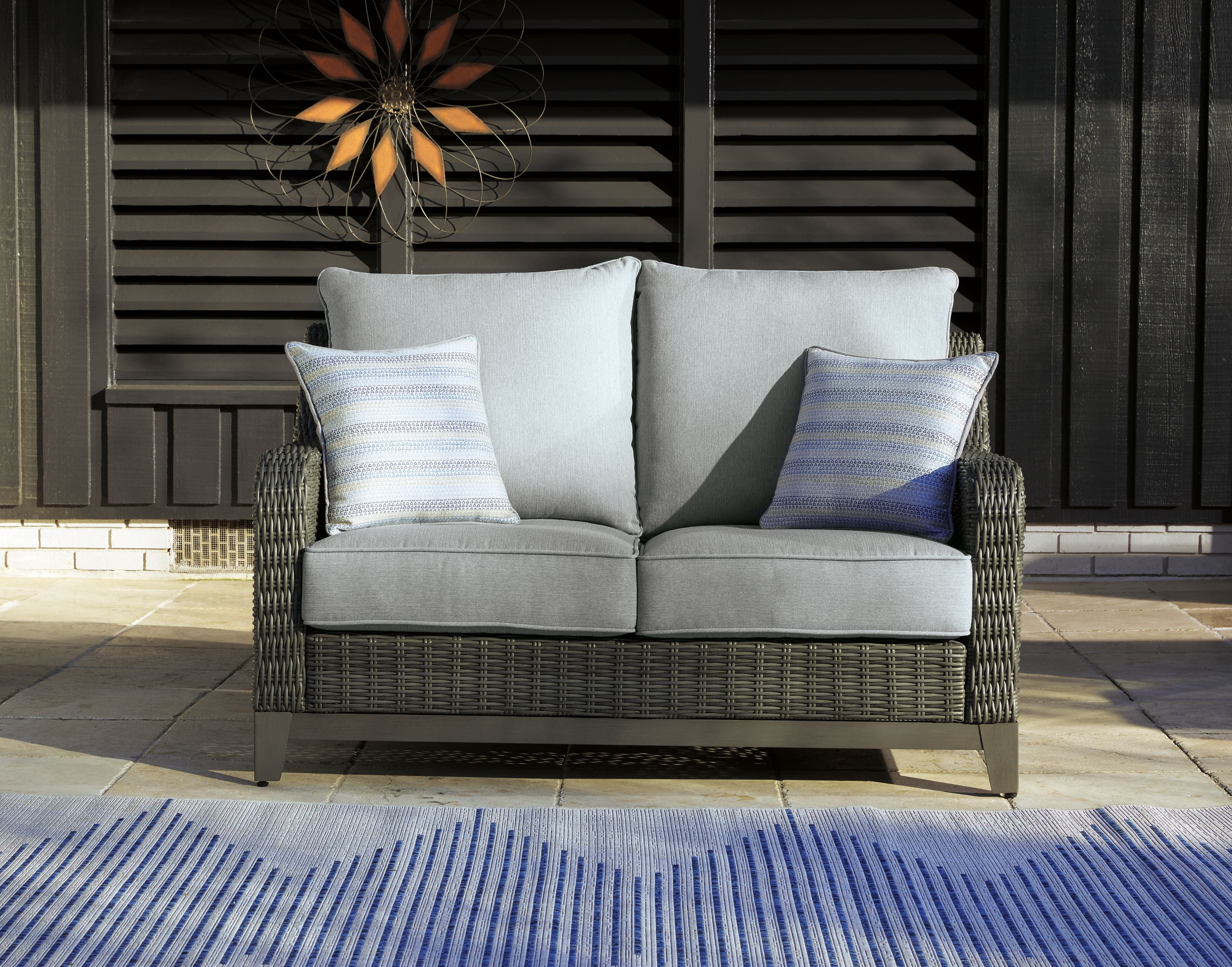 Gray wicker loveseat with seat cushions, back cushions, and patterned pillows outdoors