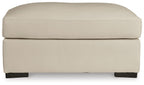 Almond padded ottoman with rounded top, visible panel stitching, and dark feet.