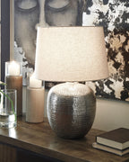 Antique silver metal table lamp with textured base and beige fabric drum shade on table