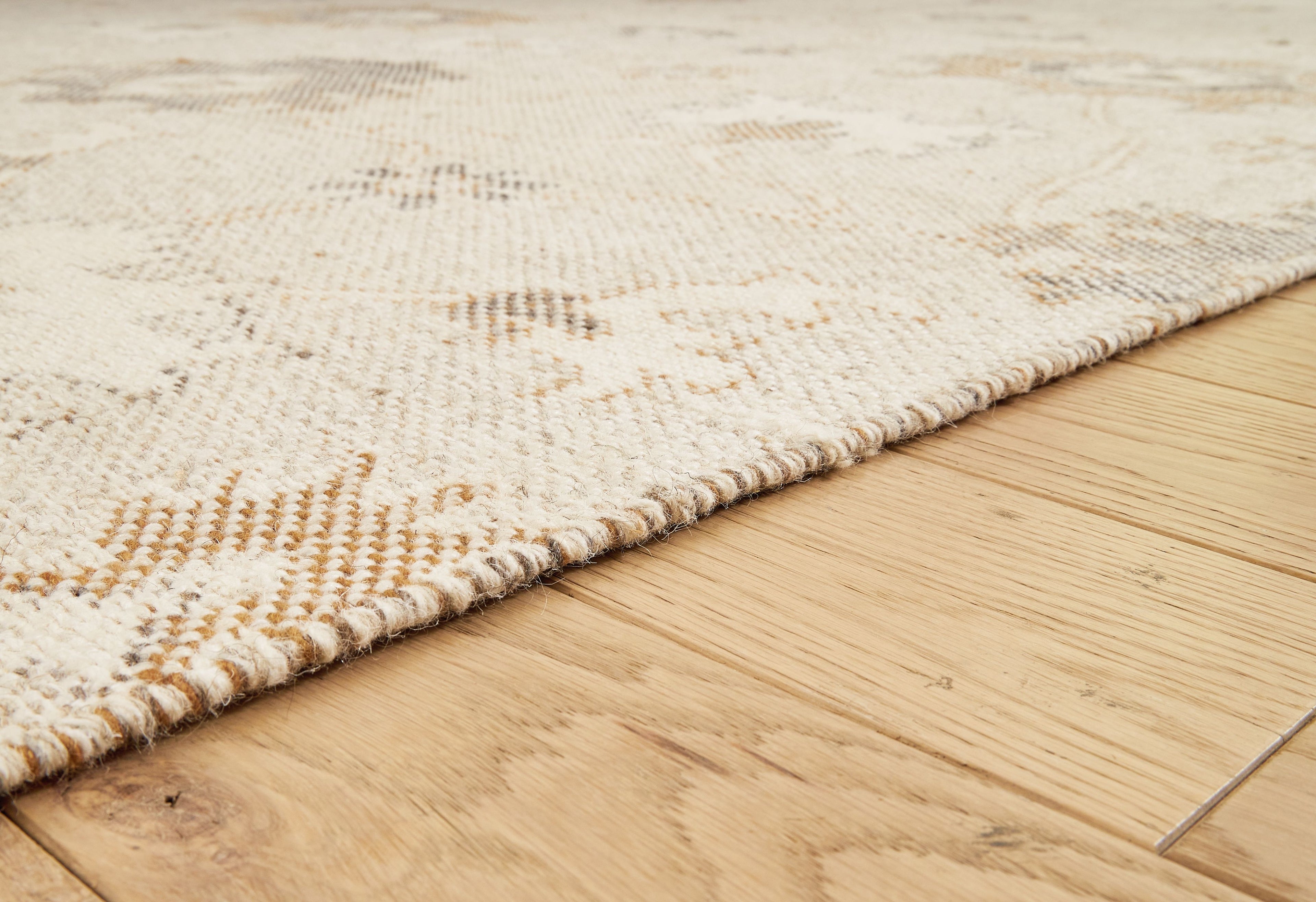 Beige rug edge close-up with textured surface and short fringed trim