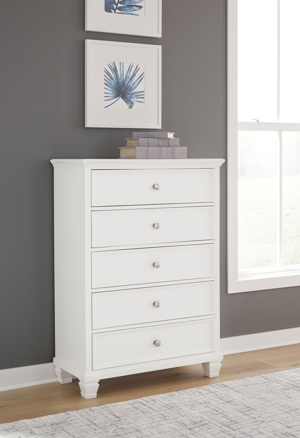 White five-drawer chest with round knobs and crown molding, standing on short legs.
