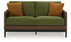 Outdoor loveseat with green seat cushions, brown woven base, and orange-brown back pillows