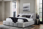 Gray upholstered bed with tall headboard and quilted panels, pillows and blankets