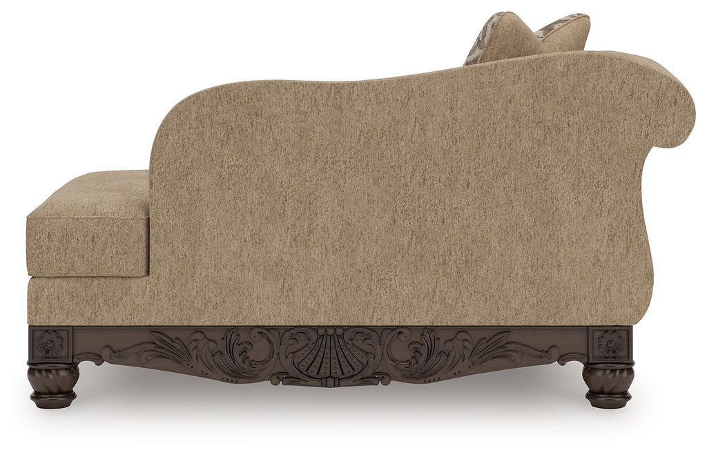 Beige corner chaise with curved back, patterned pillow, dark carved wooden base.
