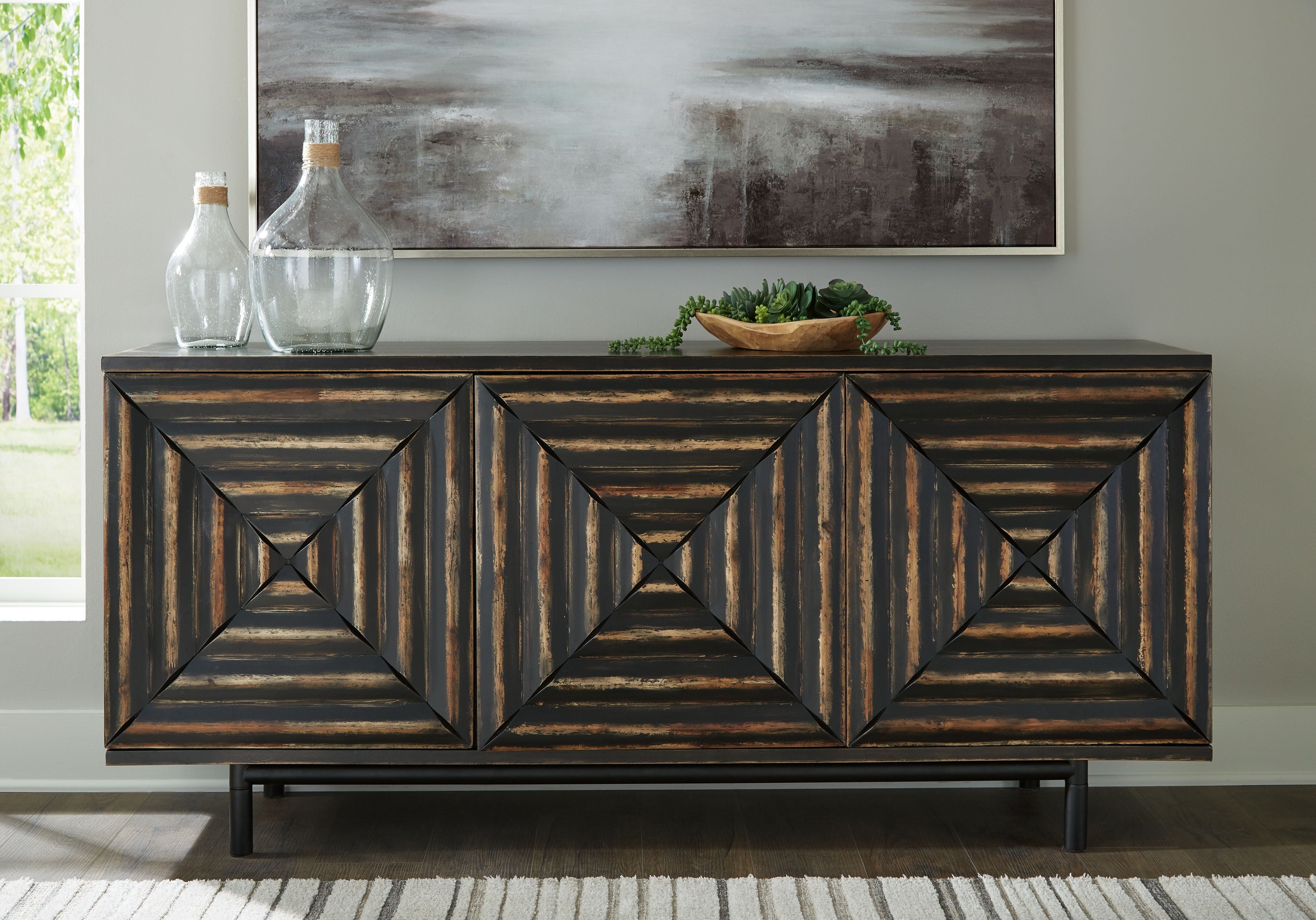 Distressed black accent cabinet with three paneled doors and geometric carved center.