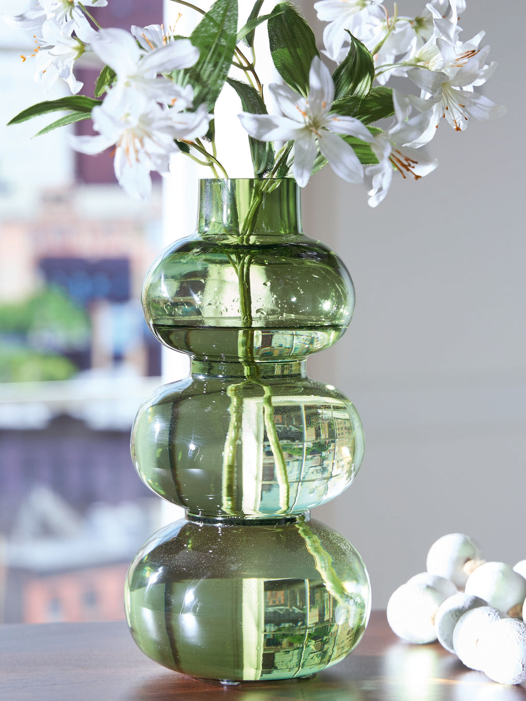Green glass vase with stacked rounded sections holding white flowers.