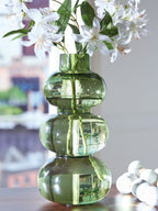 Green glass vase with stacked rounded sections holding white flowers.