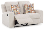 Reclining loveseat with light beige upholstery and patterned pillows, reclined seat