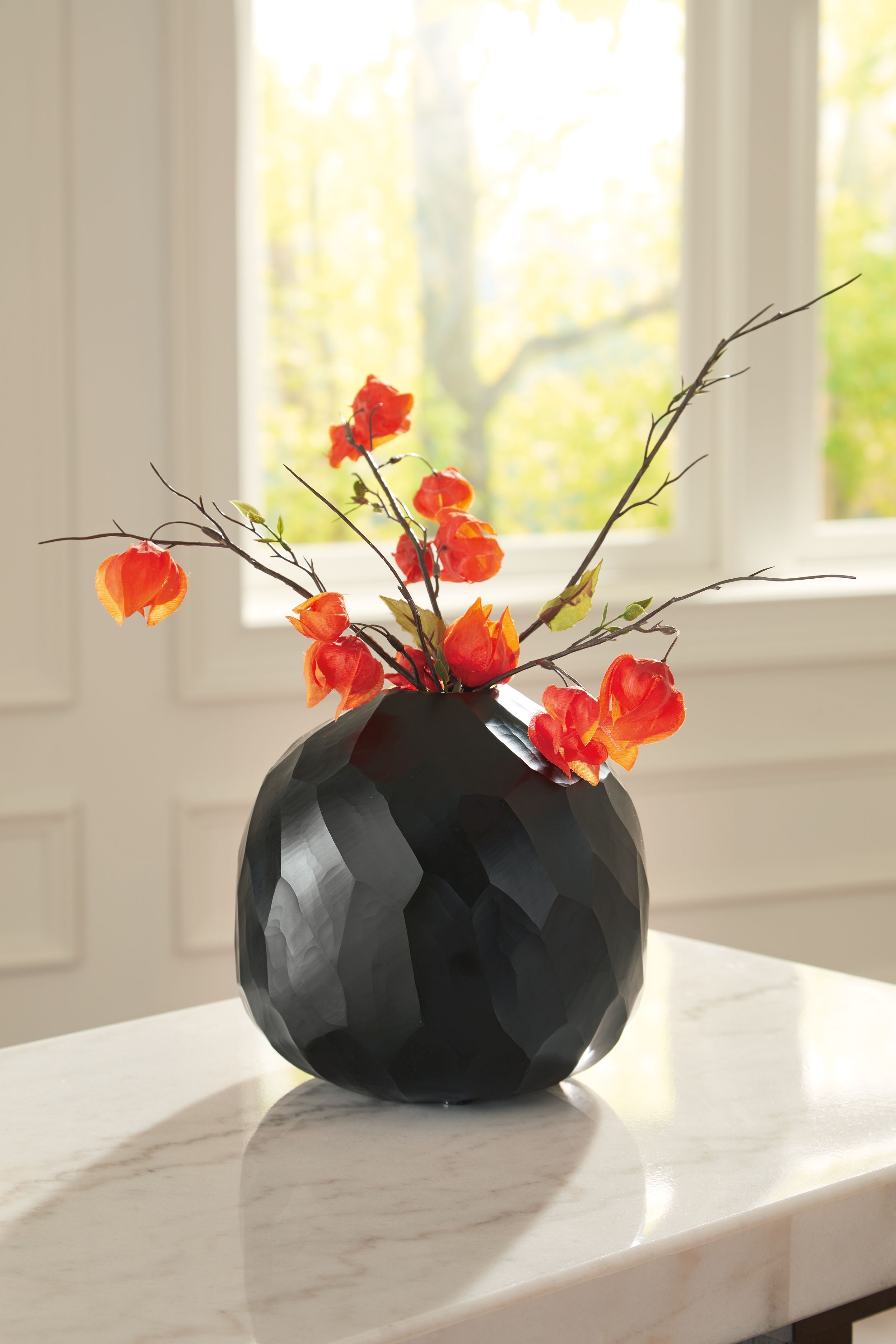 Black faceted vase holding red flowers with slim stems