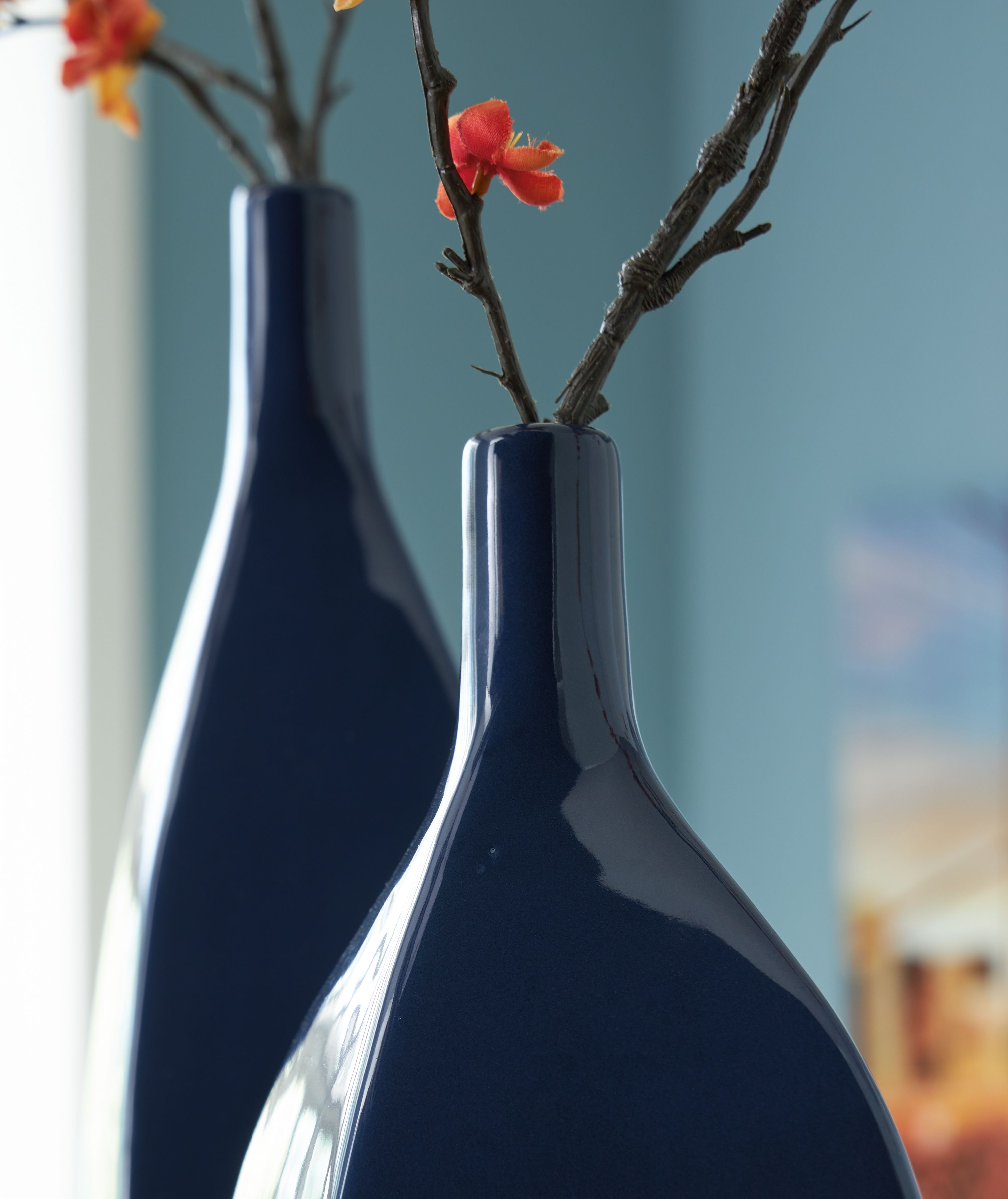 Close-up of glossy blue ceramic vase with stems and small blossoms