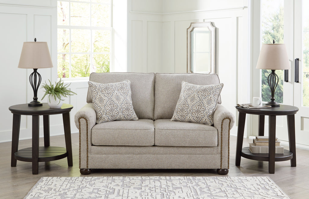Light gray-beige loveseat with two patterned pillows, rolled arms, and nail trim