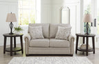 Light gray-beige loveseat with two patterned pillows, rolled arms, and nail trim