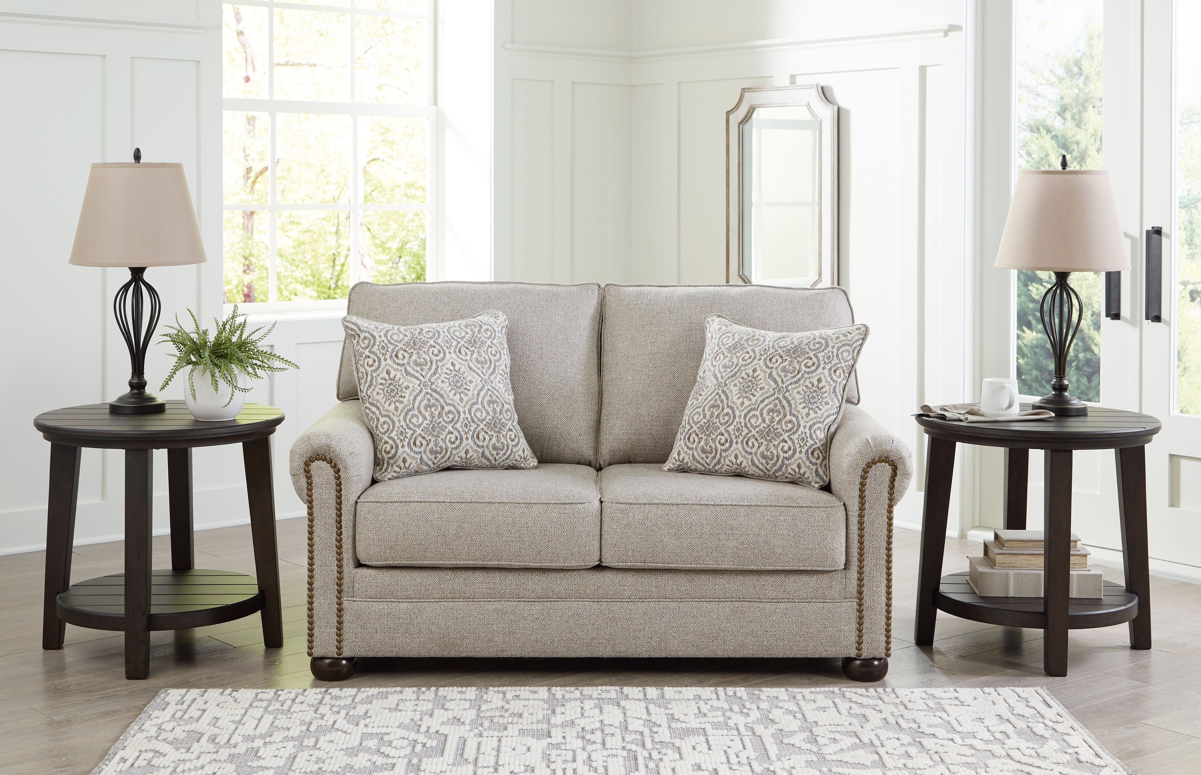 Light gray-beige loveseat with two patterned pillows, rolled arms, and nail trim
