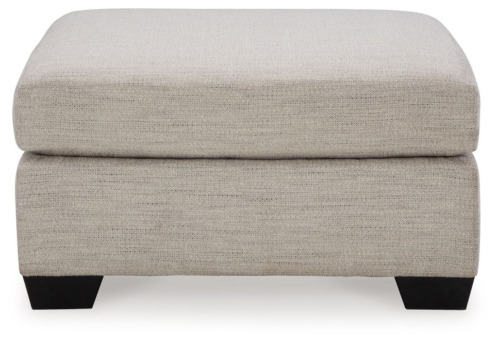 Oversized ottoman with light beige fabric, thick cushioned seat and squared black legs.