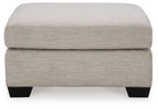 Oversized ottoman with light beige fabric, thick cushioned seat and squared black legs.