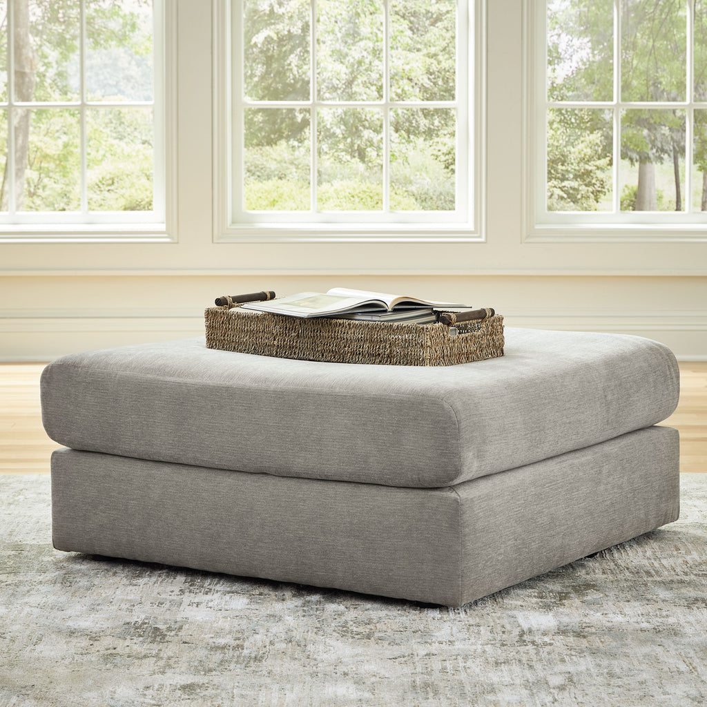 Upholstered ash-gray ottoman with rounded corners; open book on top